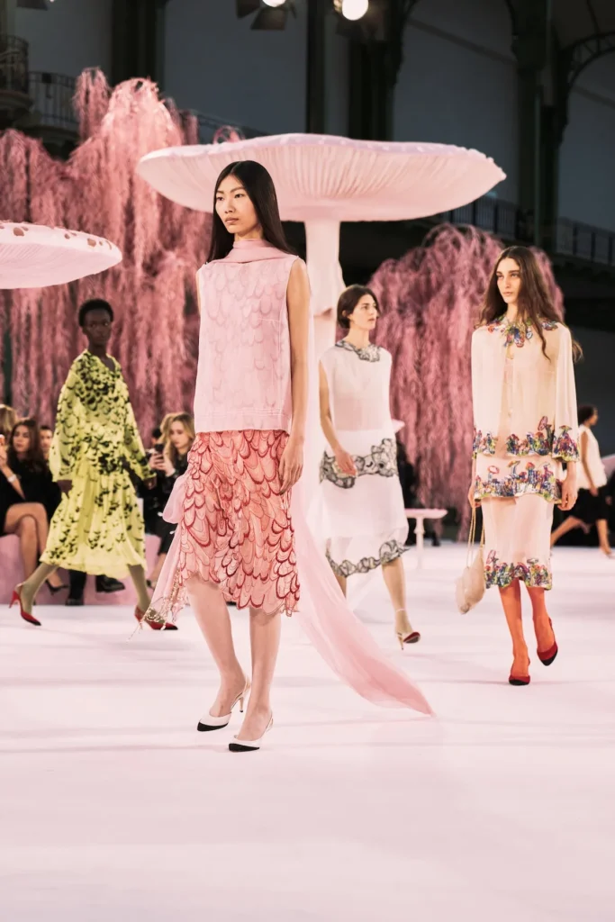 Fotografia z prehliadky Chanel SS 2026 v Paríži, kde Matthieu Blazy debutoval ako kreatívny riaditeľ. Modelky prezentujú tweedové kostýmy, pastelové scenérie a surrealistické prvky inšpirované literatúrou a popkultúrou.