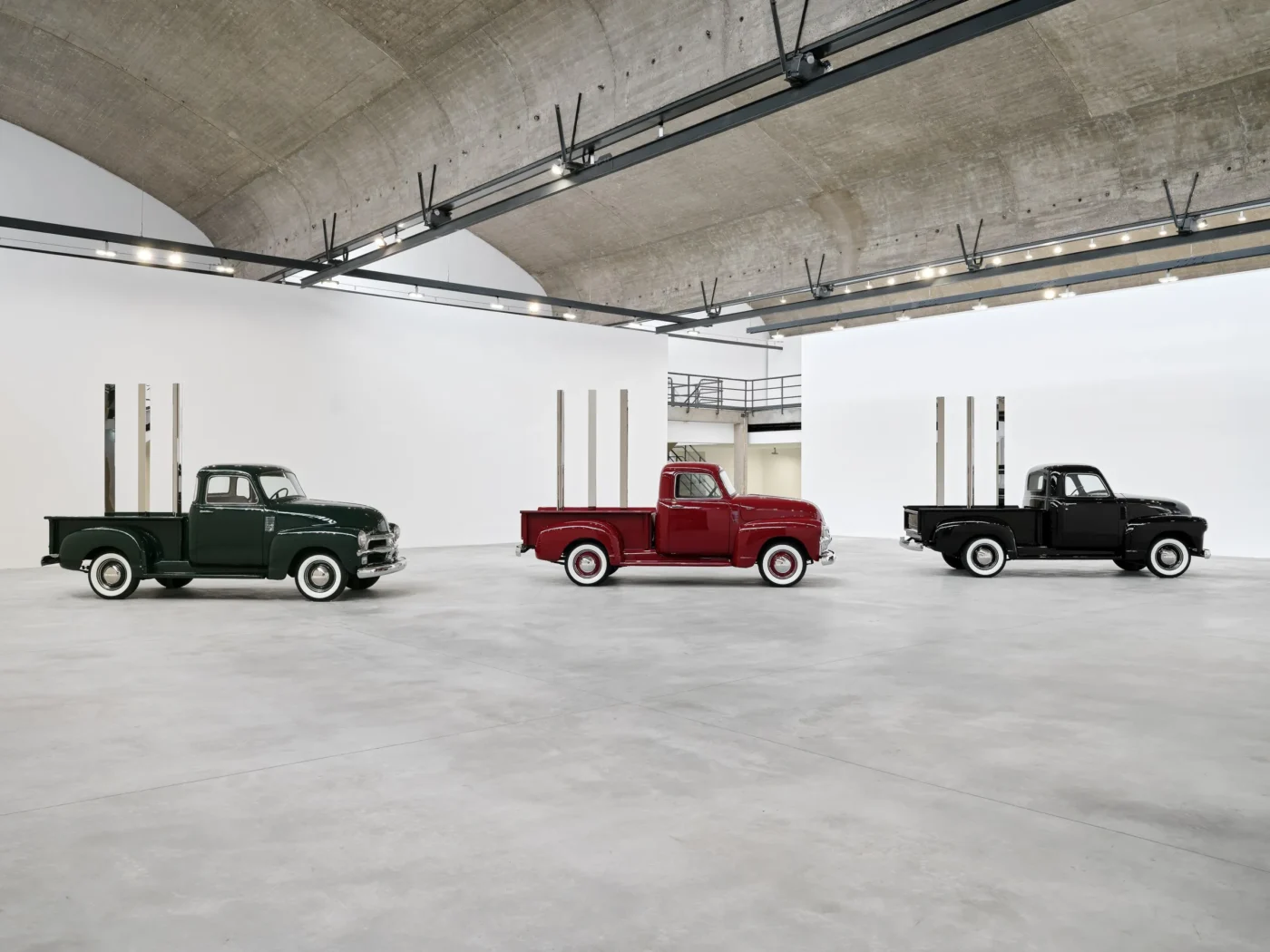 Tri vintage nákladiaky Chevrolet z roku 1950 v zelené, červenej a čiernej farbe s geometrickými tyčami na korbe, inštalačný pohľad, Gagosian Le Bourget, Paríž