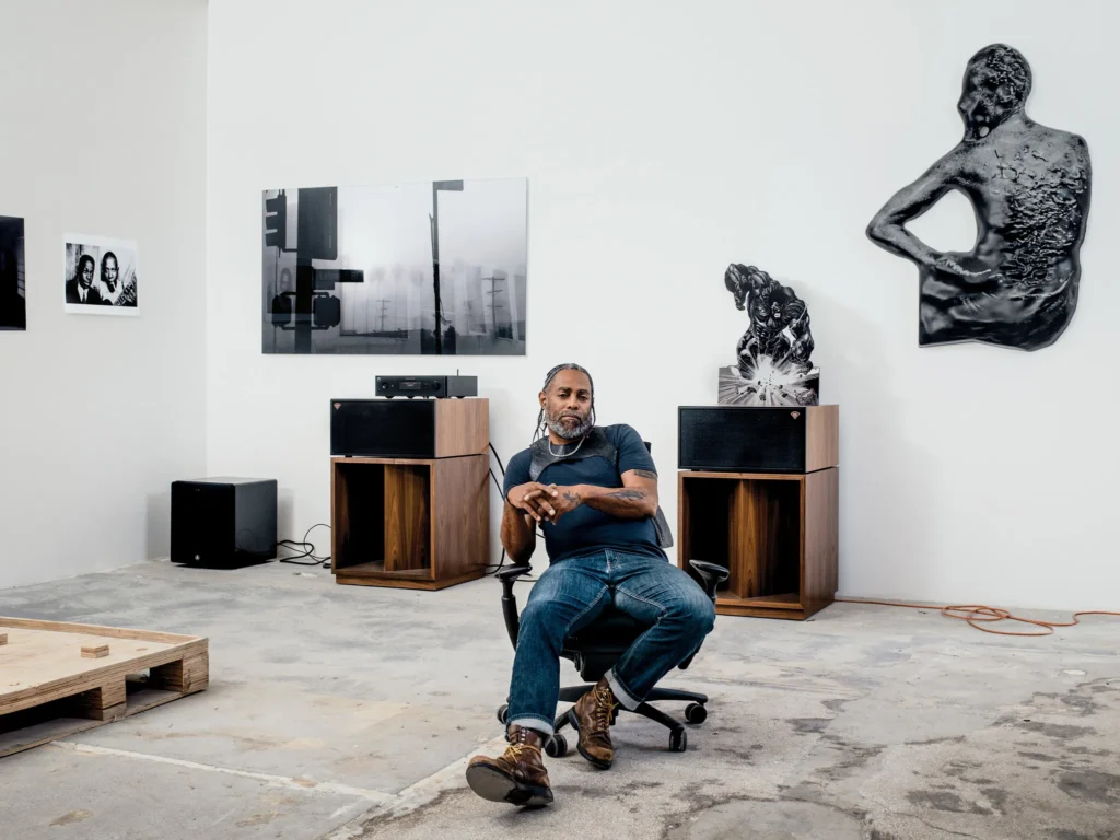 Art Basel Awards 2026 — Arthur Jafa sedí v ateliéri obklopený svojimi dielami, vrátane sochy Ex-Slave Gordon 2017 a videa Love Is the Message.