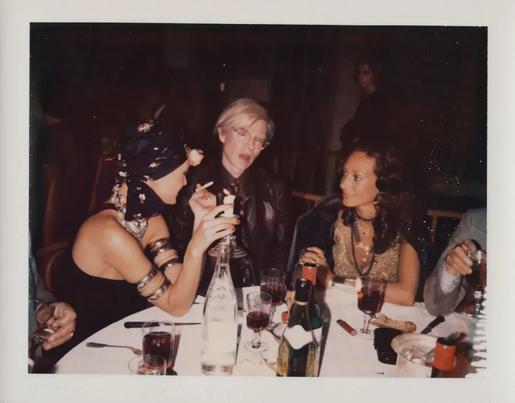 Saint Laurent Warhol — Loulou de la Falaise, Andy Warhol a Marisa Berenson pri večeri, 1972, farebná fotografia.