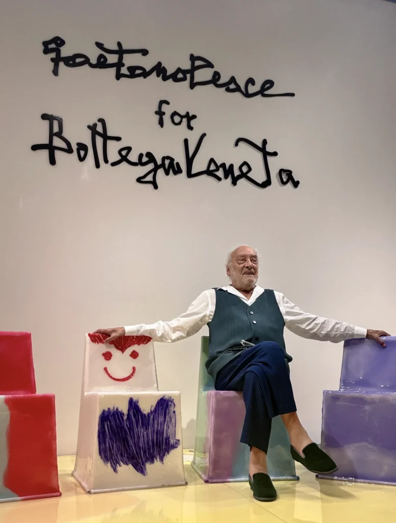 Gaetano Pesce sedí medzi farebnými plastovými stoličkami s detskými kresbami v priestore Bottega Veneta.
