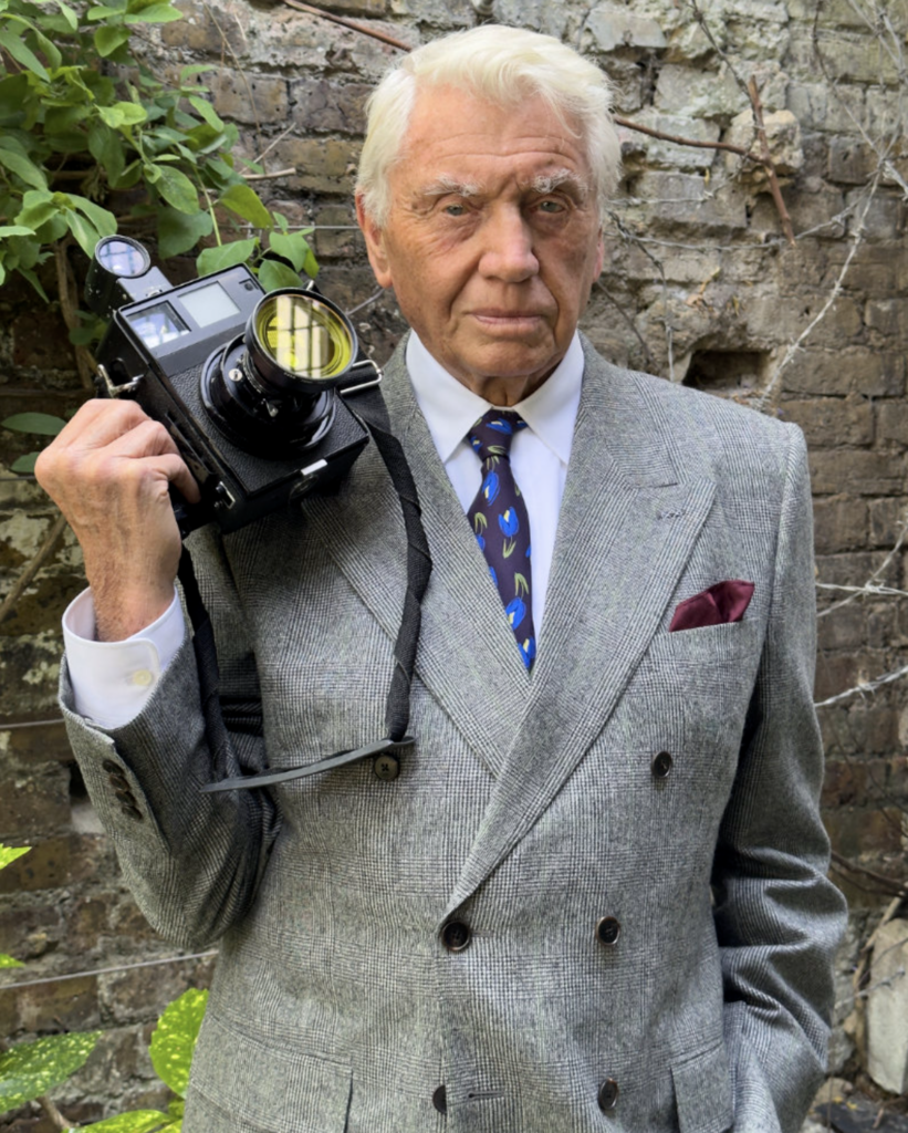 Alt text:
Don McCullin v tvídovom obleku Givenchy s fotoaparátom, kampaň Spring Summer 2027