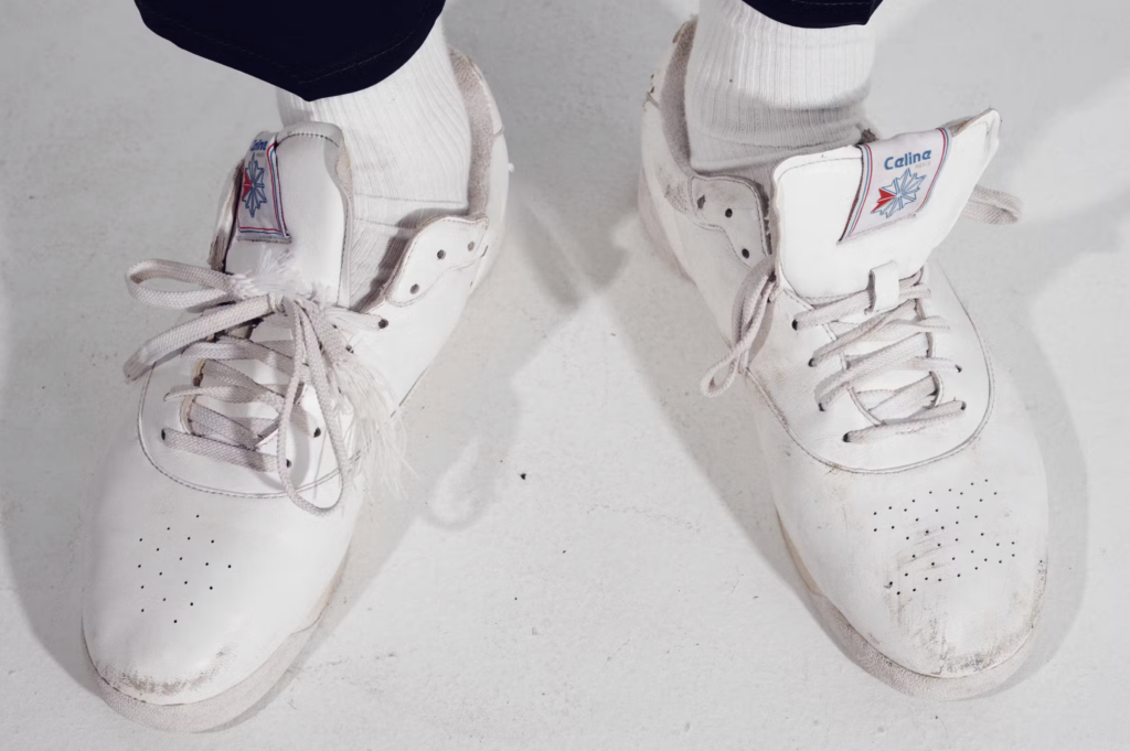 Detail bielych tenisiek z kolaborácie Celine a Reebok s logom Celine na jazyku, zámerne zostarnutý vzhľad kože