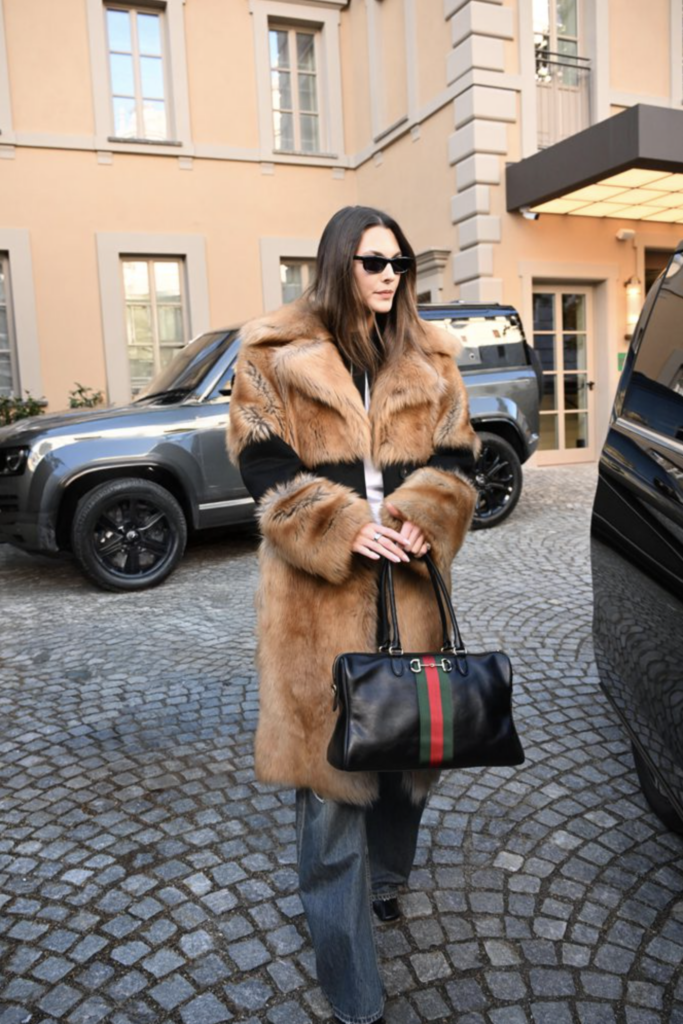 Talianska modelka Vittoria Ceretti na dláždenej ulici s čiernou kabelkou Gucci Borsetto Large Boston Bag, oblečená v hnedej kožušinovej bunde a širokých džínsoch
