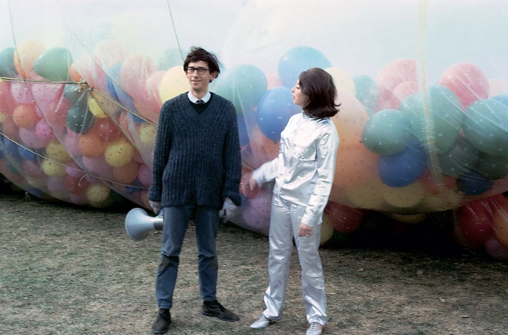 Christo a Jeanne-Claude stoja pred obrovskou priehľadnou fóliou naplnenou farebnými balónmi, inštalácia 42,390 Cubic Feet Package v Minneapolise v roku 1966