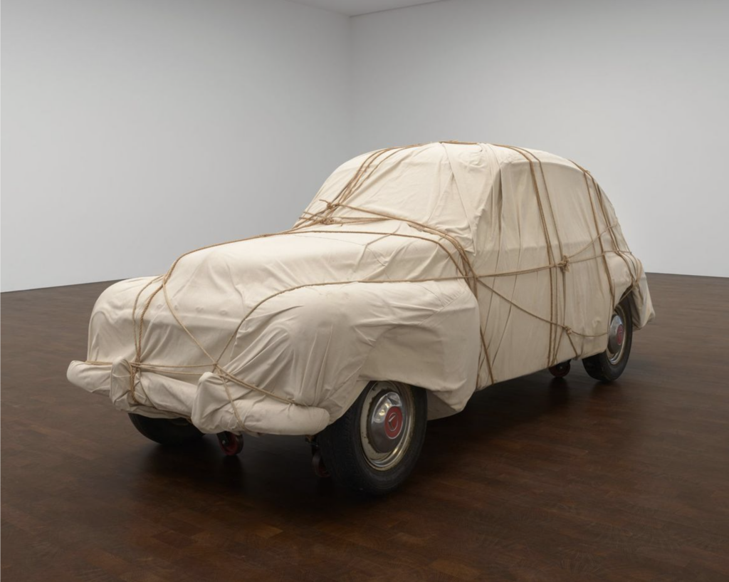 Volvo PV-544 zabalené v béžovej látke previazanej lanom v galerijnom priestore, dielo Wrapped Automobile od Christa z roku 1981