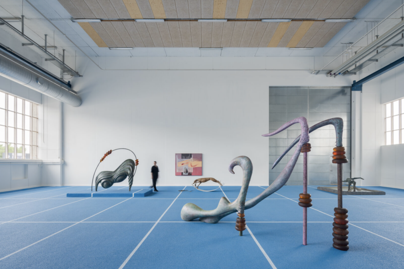 Inštalačný pohľad na výstavu Camille Henrot Paper Planes v Copenhagen Contemporary s bronzovými organickými sochami na modrom koberci a maľbami na stenách