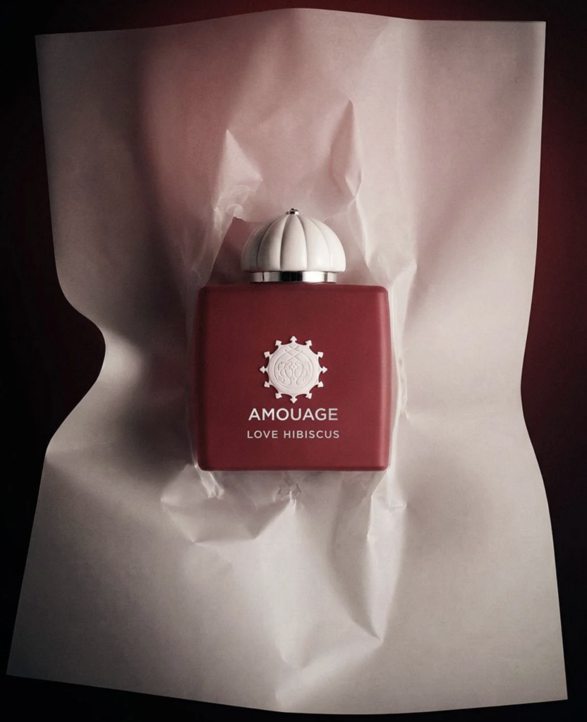 Flakón parfumu Amouage Love Hibiscus fotografovaný z nadhľadu na zmačkanom bielom papieri s tmavým pozadím