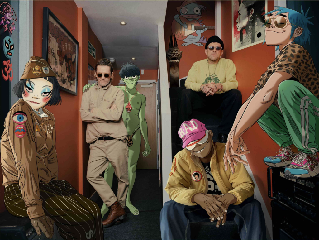 Propagačná fotografia Gorillaz zo Song Machine Season One, animovaní členovia 2-D, Murdoc, Noodle a Russel sedia na gauči spolu so skutočnými hudobníkmi v hudbou vyplnenej miestnosti