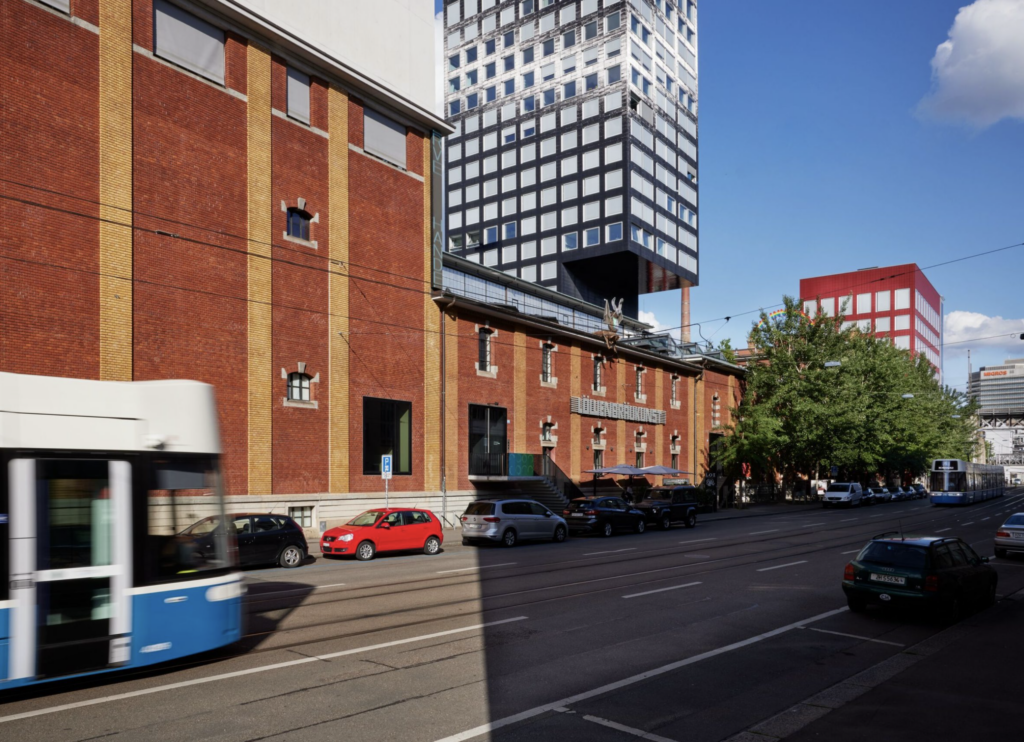Presklený interiér pobočky Hauser & Wirth na Bahnhofstrasse v Zürichu, žena prechádza popri veľkých sochách, medzi nimi hnedej diskovej soche a bielej svetelnej inštalácii