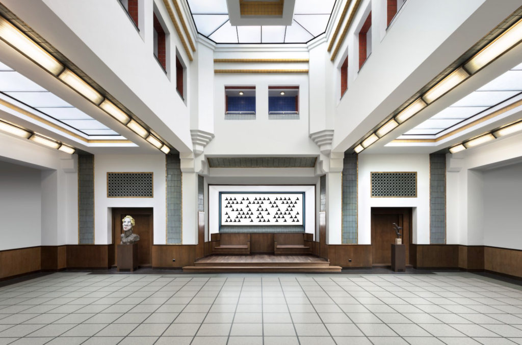 Vysoká sieň Kunstmuseum Den Haag so svetlíkom v strope, po stranách výklenky s bustou a sochou, uprostred veľkoformátové čiernobiele dielo Bridget Riley