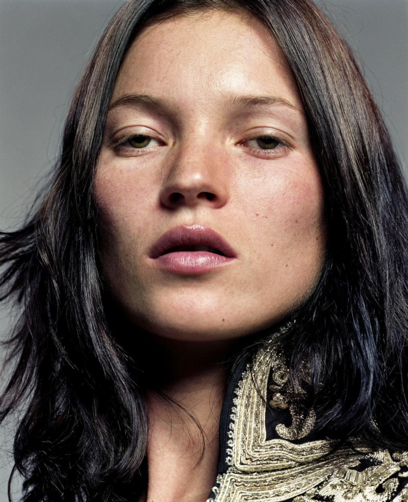 Extrémny detail tváre Kate Moss, pootvorené pery, priamy pohľad do kamery, jemné svetlo zdôrazňujúce textúru pokožky