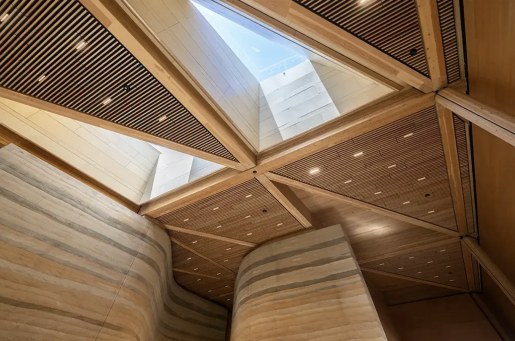 Pohľad zdola na geometrickú drevenú strešnú konštrukciu Roosevelt Presidential Library so svetlíkom v strede, obklopenú vlnitými hlinenými stĺpmi s farebnými vrstvami