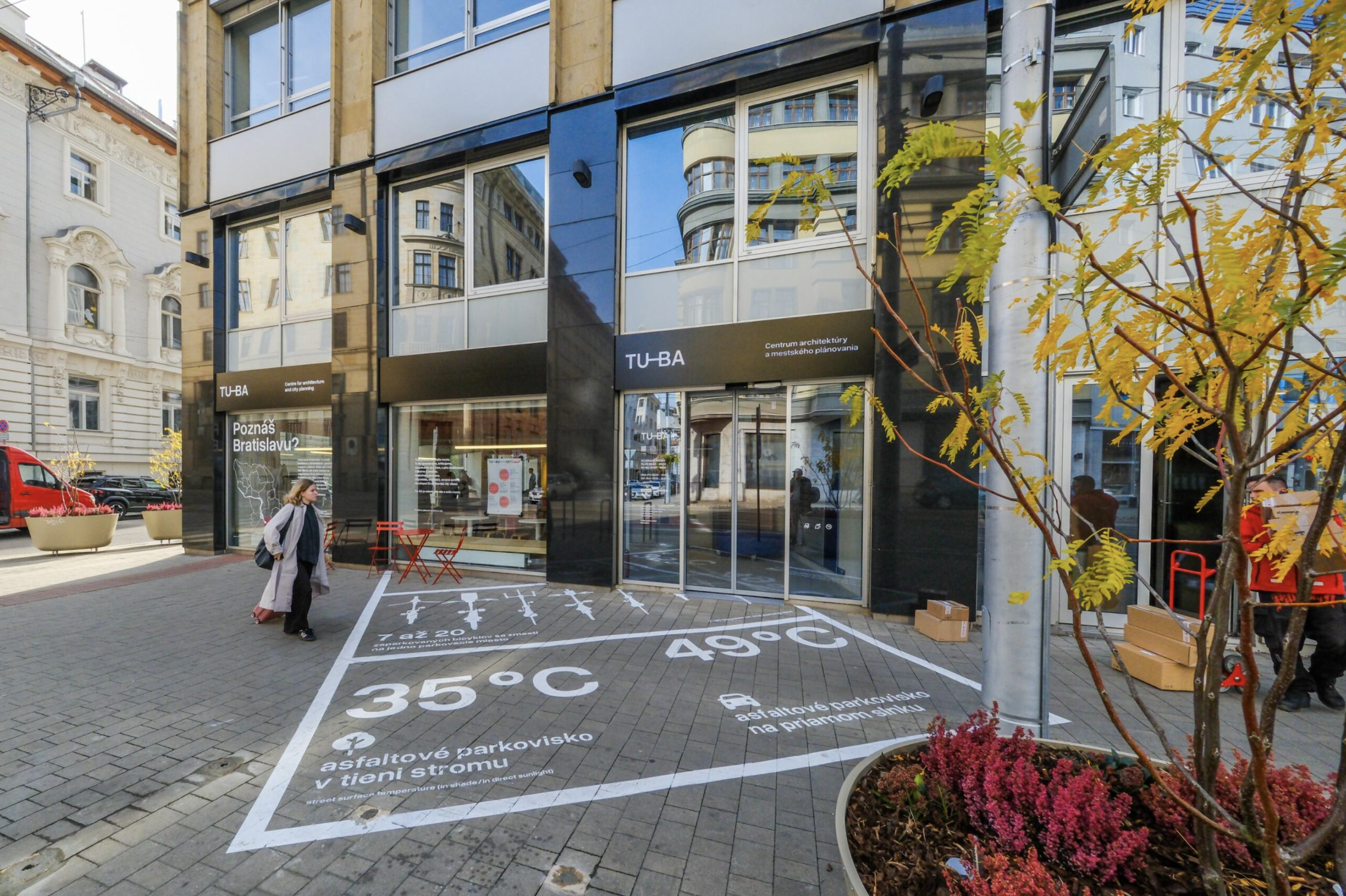 Vstup do centra TU-BA na rohu ulíc Štúrova a Medená, na chodníku pred budovou je nakreslená vizualizácia teploty asfaltového parkoviska v tieni a na priamom slnku

