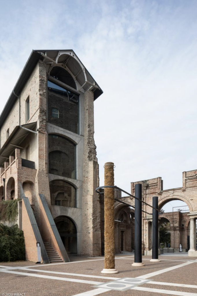 Historická veža Manica Lunga v Castello di Rivoli, rekonštruovaná tehlová stavba s presklenou strešnou konštrukciou a kovovým schodiskom, obklopená stĺpmi a ruinami