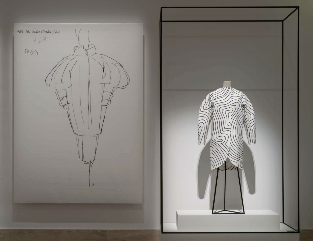 Inštalačný pohľad na výstavu Fendi and Karl Lagerfeld, návrhový skicár a biele šaty s líniovým vzorom vo vitríne, Galleria Nazionale d'Arte Moderna e Contemporanea, Rím
