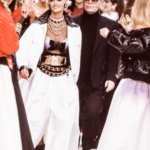Karl Lagerfeld kráčajúci po móle po boku modelky v bielom kostýme s reťazovým opaskom Chanel, počas přehliadky Chanel
