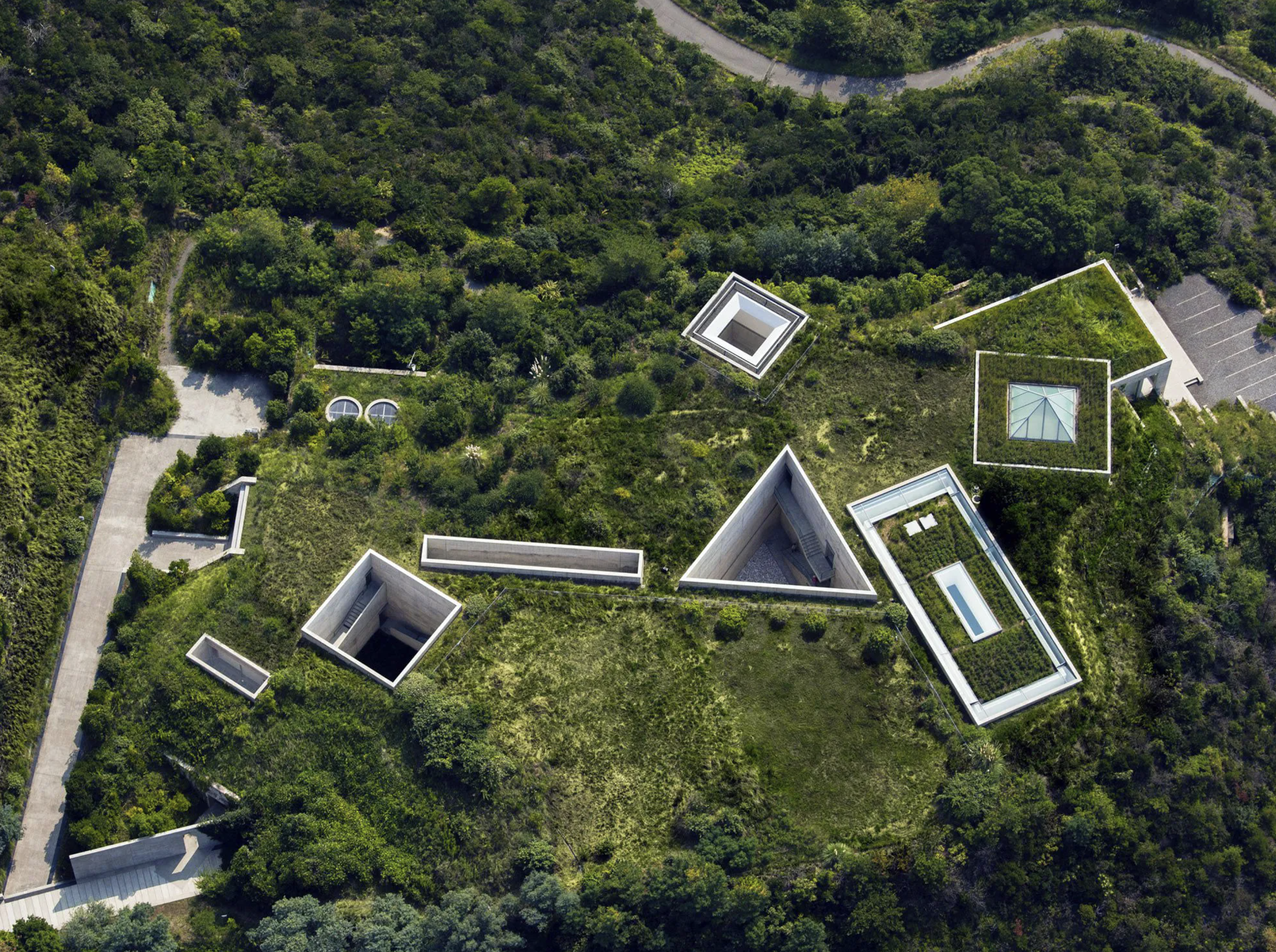 Letecký pohľad na múzeum Chichu na ostrove Naošima, s geometrickými betónovými dvormi a svetlíkmi zapustenými do zeleného kopca nad morom