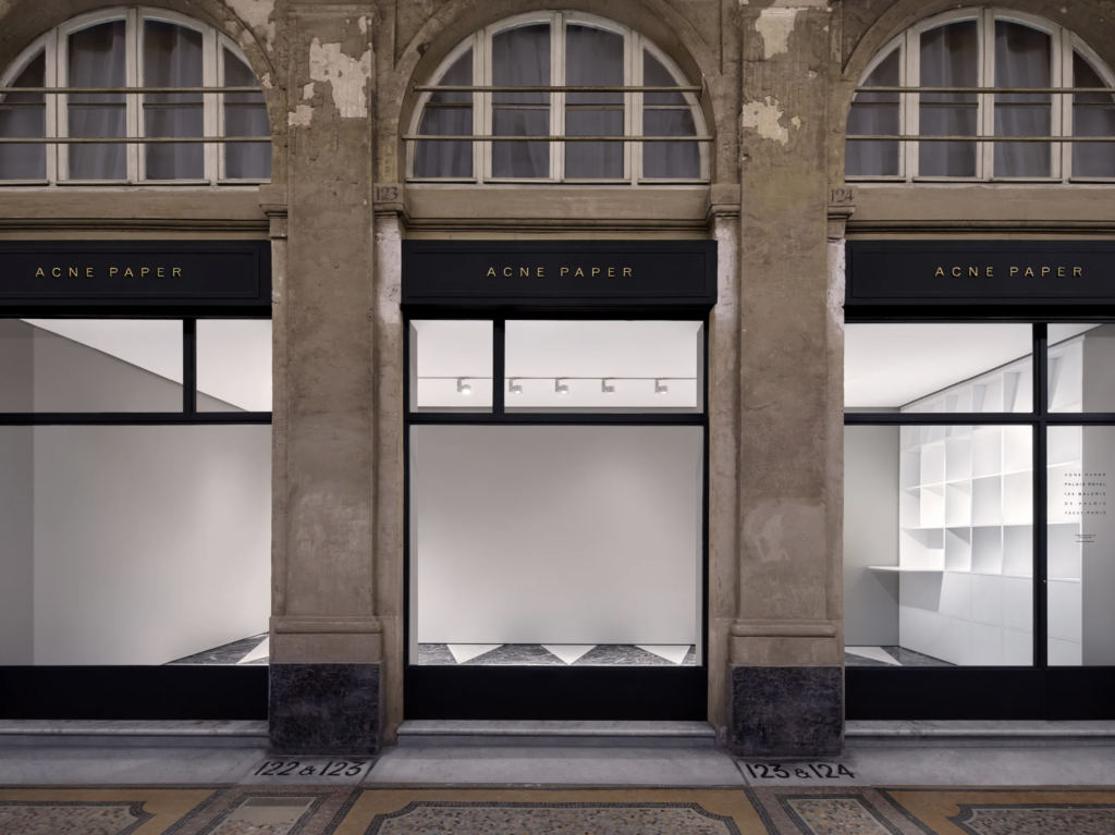 Fasáda galérie Acne Paper v parížskom Palais Royal s výkladmi orámovanými pieskovcovými pilastrami a mramorovou dlažbou v šachovnicovom vzore