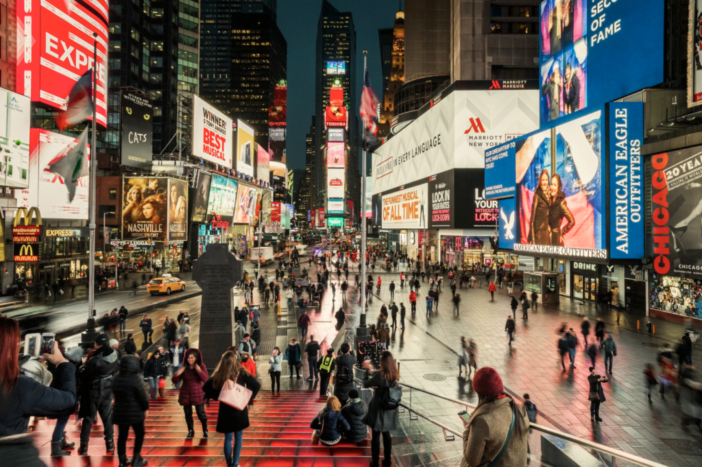 Times Square po redizajne od Snøhetty s červenými schodmi a rozsiahlou pešou zónou plnou ľudí medzi reklamnými bilbordmi