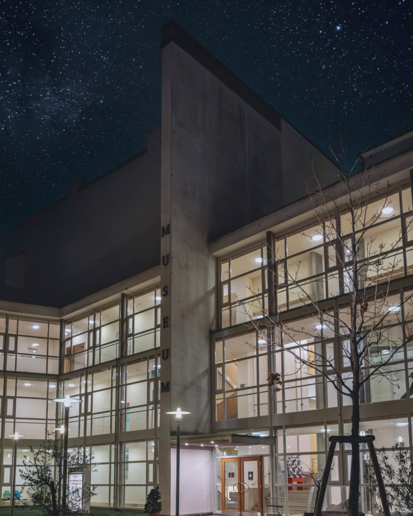 Exteriér budovy Möbelmuseum Wien v noci, presvetlené okná a nápis MUSEUM na fasáde