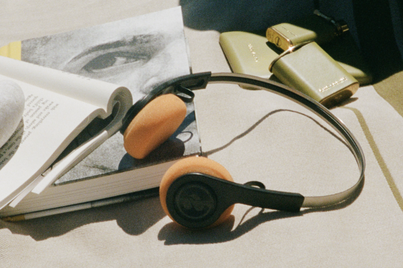 Retro slúchadlá s oranžovými vankúšikmi položené na otvorenej knihe, kampaň Saint Laurent Rive Droite Respiro