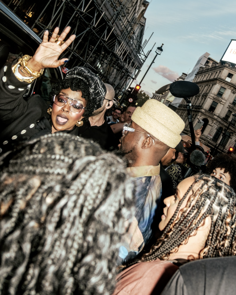 Lauryn Hill a Wyclef Jean mávajú fanúšikom z okna auta na londýnskej ulici, obklopení davom a fotografmi