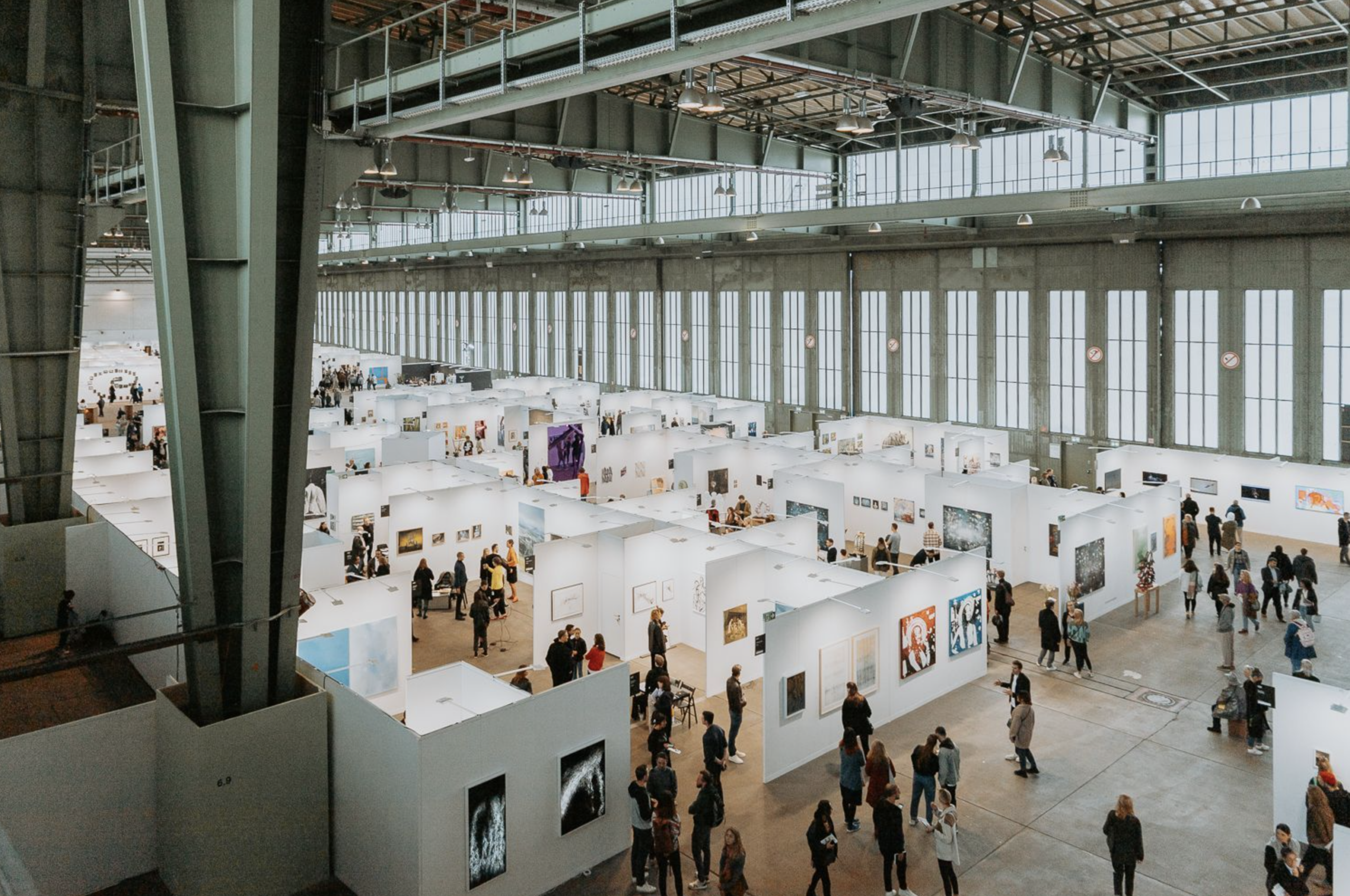 Návštevníci prechádzajú medzi galerijnými boxmi na veľtrhu POSITIONS Berlin v hangári Tempelhof