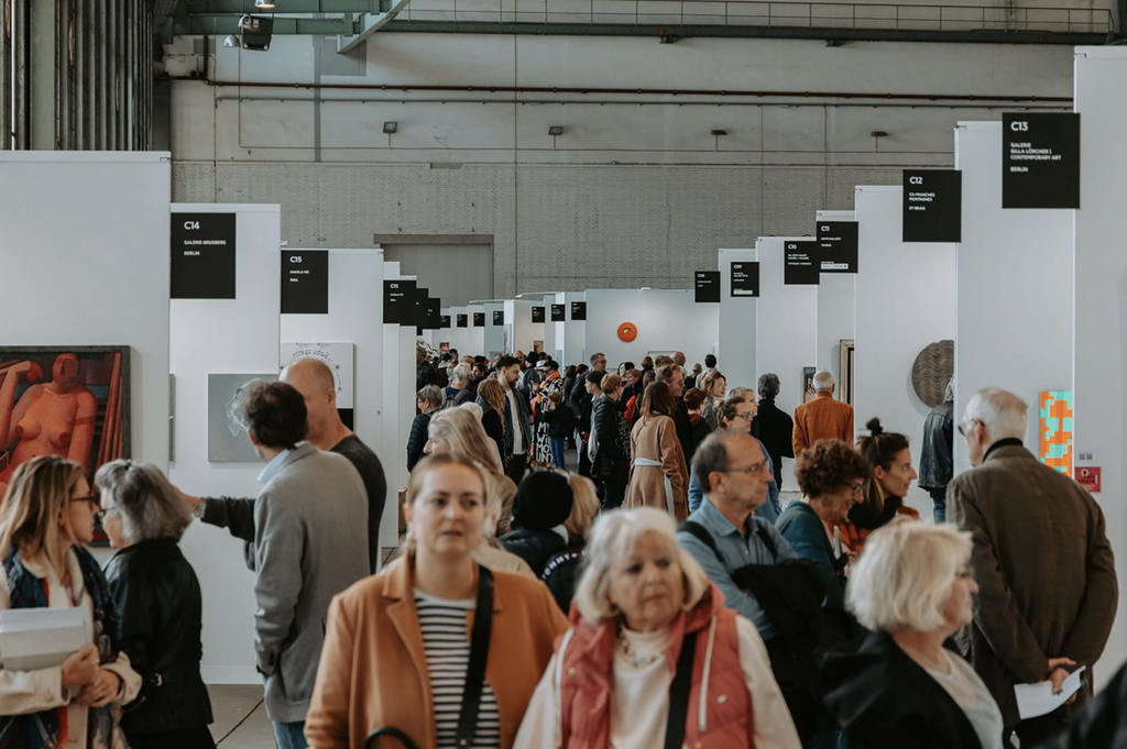 Návštevníci prechádzajú uličkou medzi galerijnými stánkami C09 až C15 na POSITIONS Berlin Art Fair