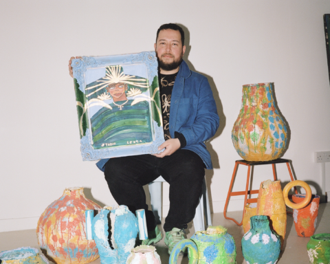 José Campos, Studio Lenca, drží maľovaný portrét obklopený farebnými keramickými nádobami