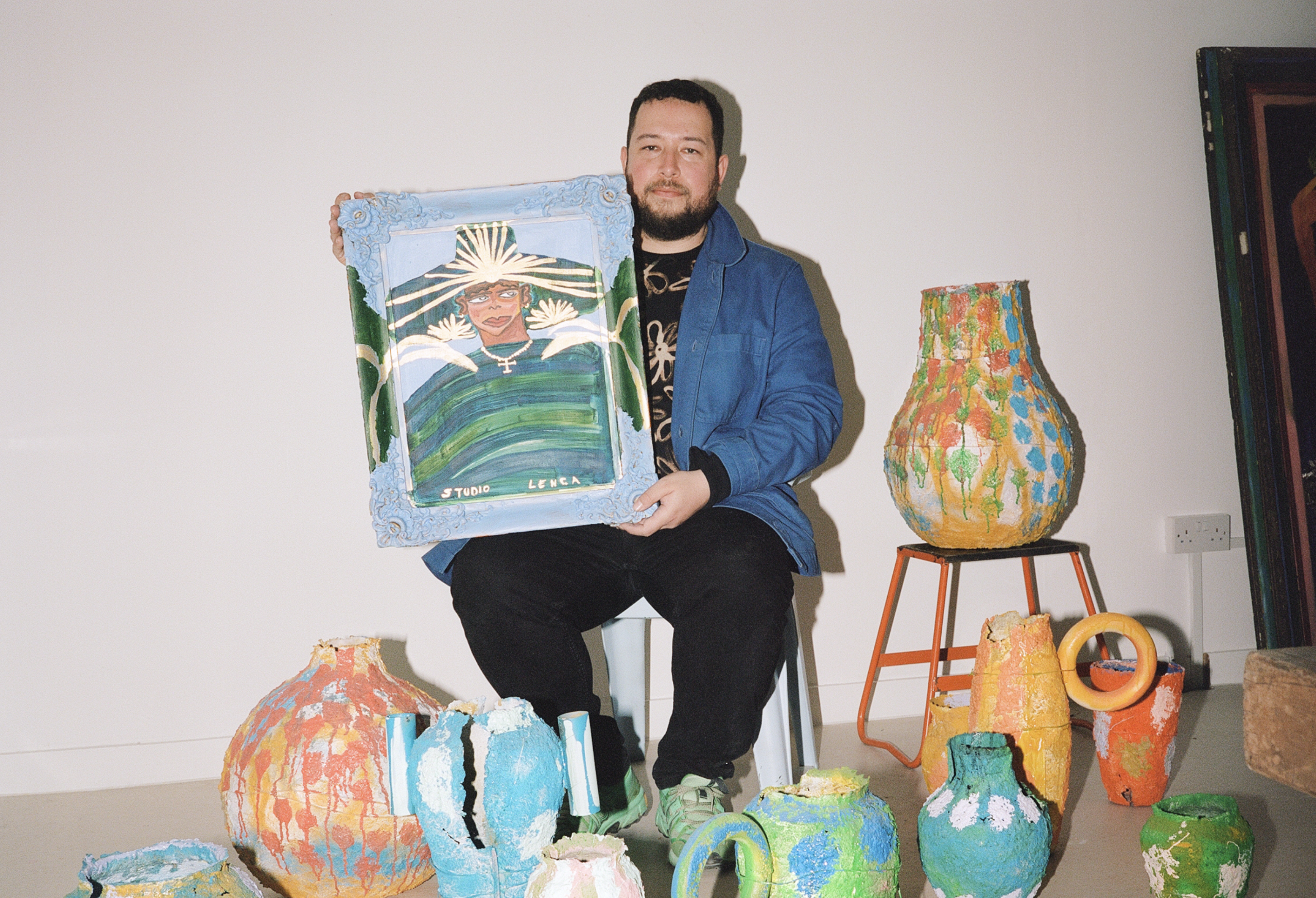 José Campos, Studio Lenca, drží maľovaný portrét obklopený farebnými keramickými nádobami