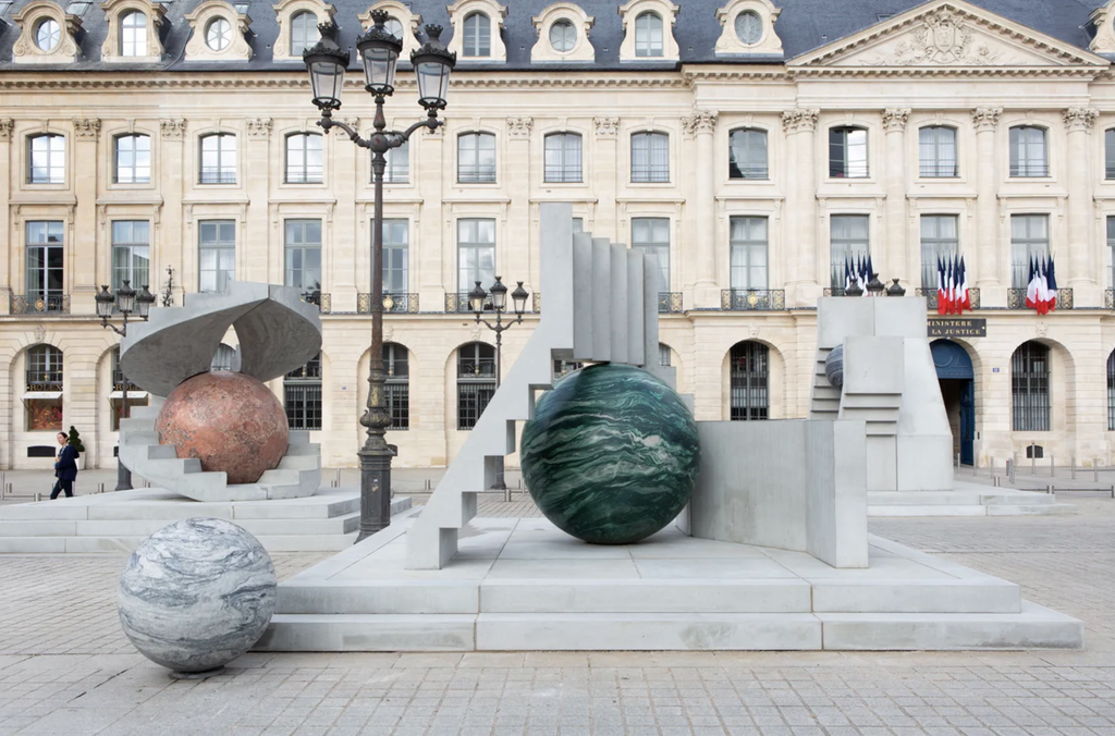 Inštalácia Alicje Kwade "Au cours des mondes" na Place Vendôme, kamenné a mramorové gule rôznych farieb na betónových schodiskových konštrukciách pred historickou fasádou.