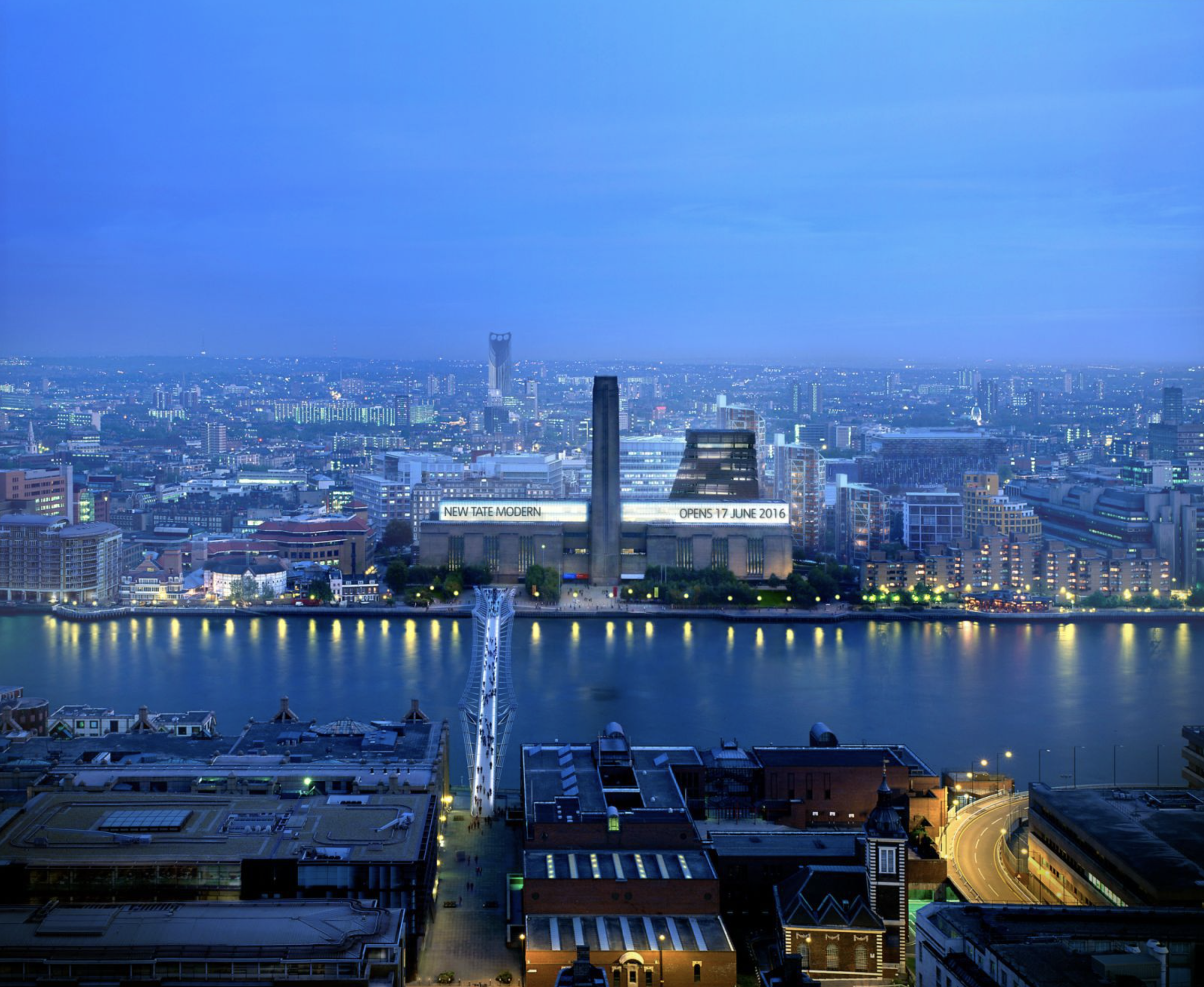 Letecký pohľad na Tate Modern v Londýne za súmraku, s charakteristickým komínom bývalej elektrárne a novou pyramídovou prístavbou od Herzog & de Meuron, rieka Temža v popredí.