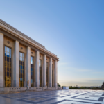Fasáda Cité de l'architecture et du patrimoine v Paríži pri západe slnka, klasicistický stĺporad s okami, v pozadí Eiffelova veža.